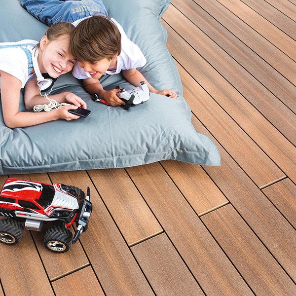 Holzfarbene Terrasse mit zwei Kindern auf einem Kissen und einem Spielzeugauto